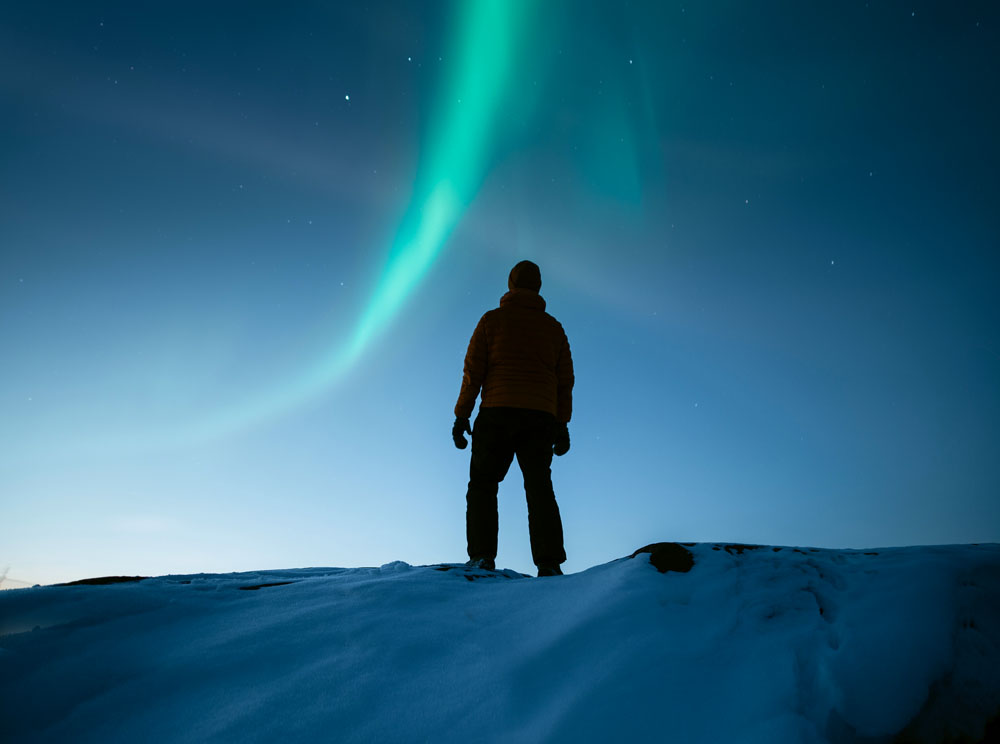 Talvimaisema, ihminen ja revontulia.